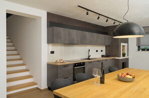 A modern kitchen with grey cabinets, a wooden countertop, and a dining area with a table set for two. - Villa Mochi (Istria - Pićan) (Pićan)