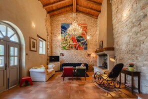 A cozy living room with a stone wall, a chandelier, a colorful abstract painting, and a fireplace. - Villa Roveria (Istria - Butkovići) (Butkovići)