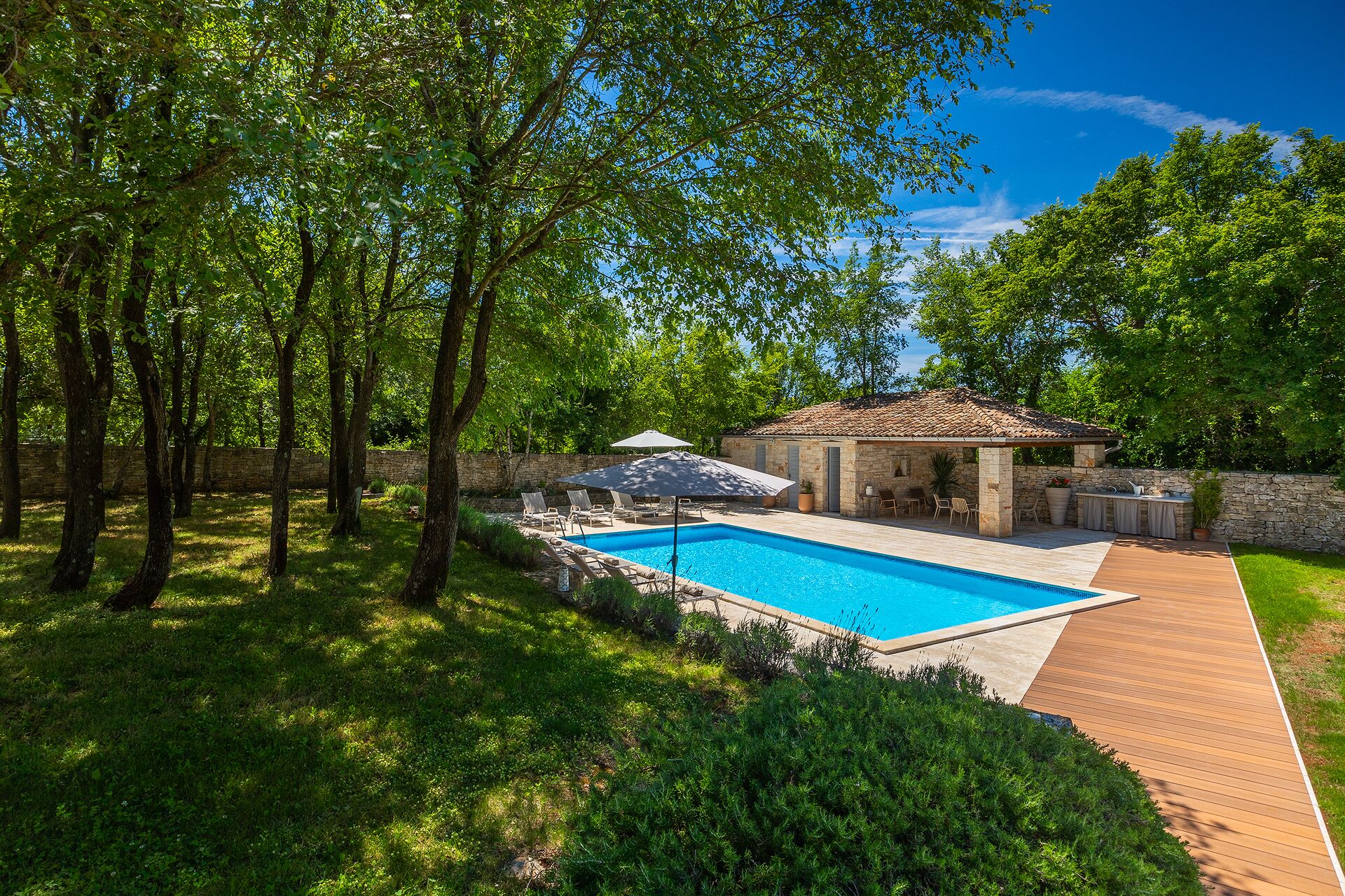 Una piscina con muelle de madera, rodeada de abundante vegetación y un muro de piedra.