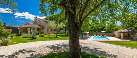 A stone house with a swimming pool, surrounded by a well-maintained lawn and a large tree.