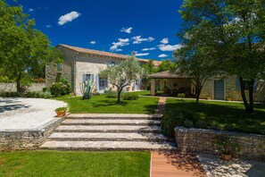 A stone building with a tiled roof, a covered patio, and a well-maintained garden with a gravel path leading to the entrance. - Villa Roveria (Istria - Butkovići) (Butkovići)