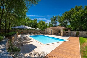 A swimming pool with lounge chairs and umbrellas, surrounded by a stone wall and greenery. - Villa Roveria (Istria - Butkovići) (Butkovići)