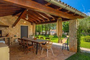 An outdoor patio with a stone wall, wooden furniture, and a view of a garden. - Villa Roveria (Istria - Butkovići) (Butkovići)