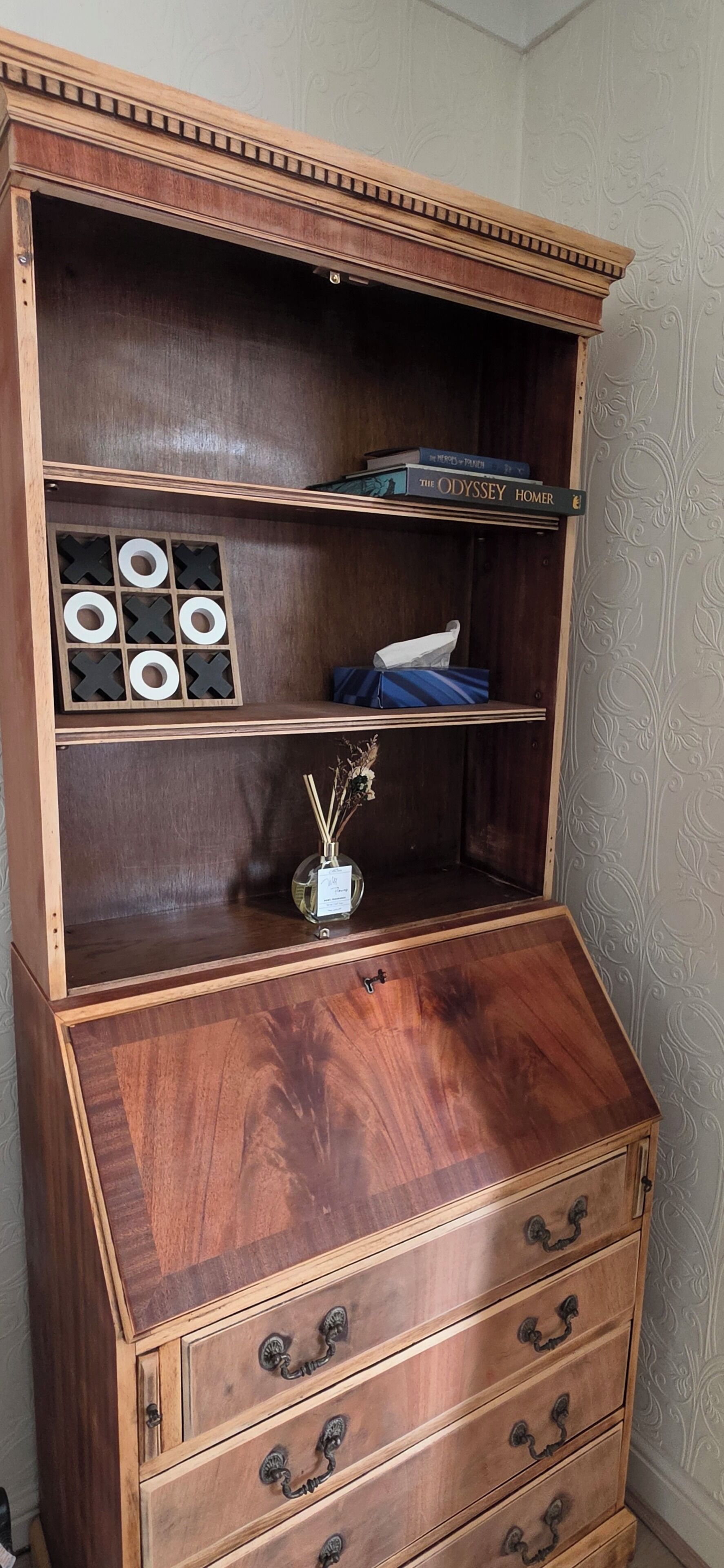 Eine Holzkommode mit mehreren Fächern, darunter ein Regal mit Büchern und eine kleine Vase mit getrockneten Blumen.