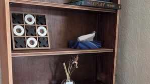 A wooden chest of drawers with multiple compartments, including a shelf with books and a small vase with dried flowers.