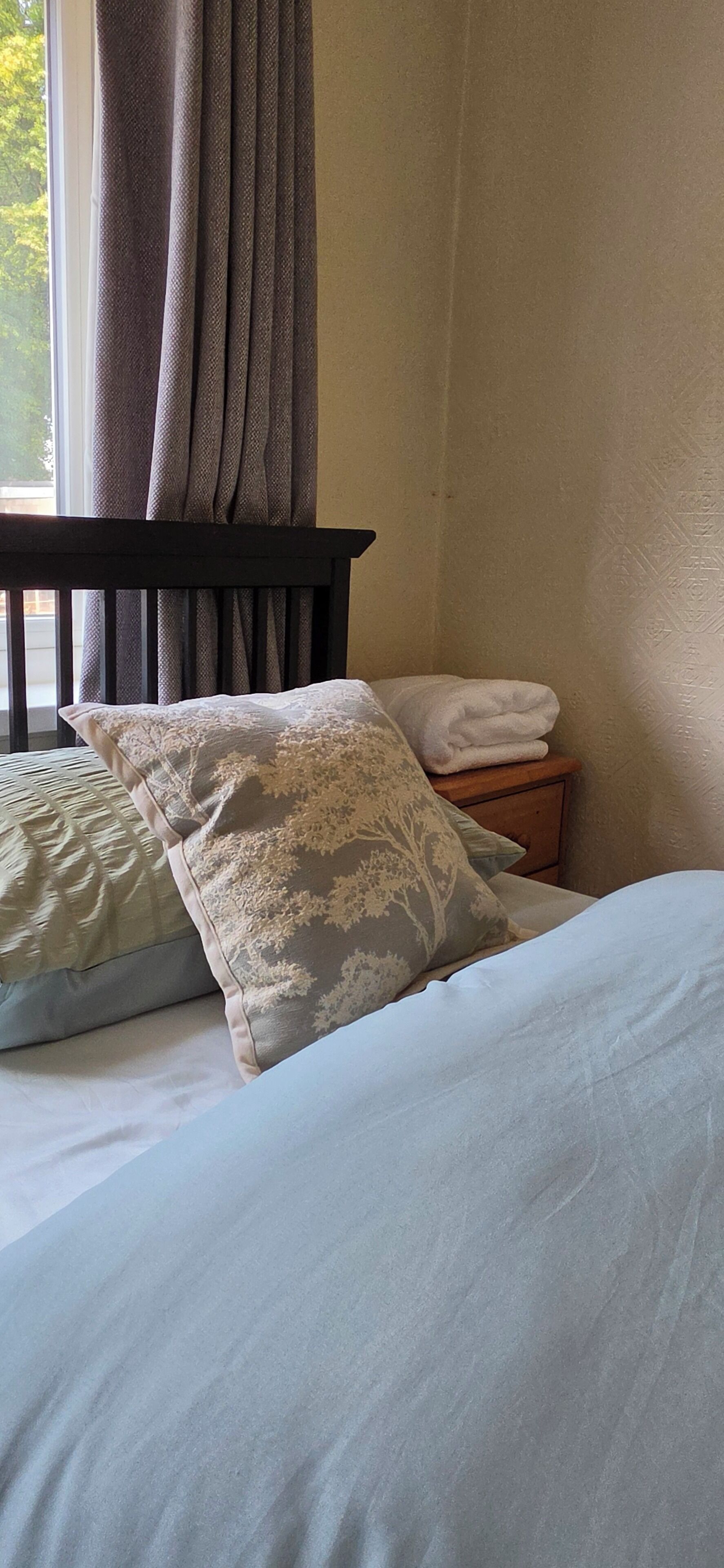 Ein Schlafzimmer mit Bett, Kissen, einem Nachttisch und einem Fenster mit Vorhängen.