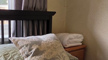 Ein Schlafzimmer mit Bett, Kissen, einem Nachttisch und einem Fenster mit Vorhängen.