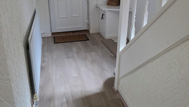 A hallway with a wooden floor, white walls, a white door with a window, and a staircase with white balusters.