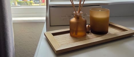 A small table with a candle and reed diffuser in a room with a window.