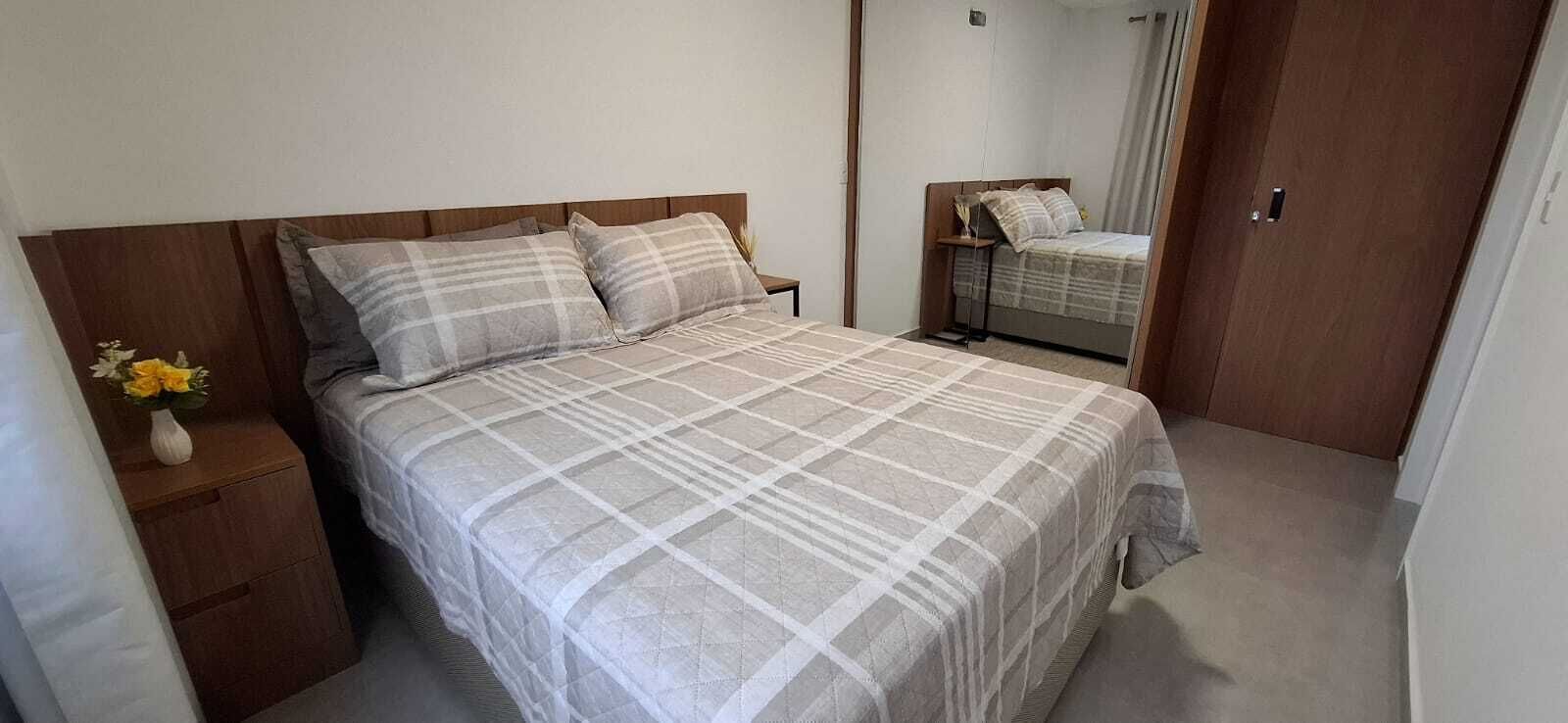 A bedroom with a bed, a nightstand, a vase with flowers, and a mirror.