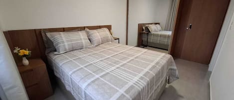 A bedroom with a bed, a nightstand, a vase with flowers, and a mirror.