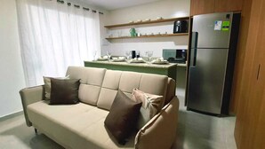 Ein Wohnzimmer mit einer Couch, einer Küchenzeile inklusive Kühlschrank und einem Esstisch mit Tellern und Gläsern.