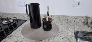 Une cuisine équipée d’une cuisinière à gaz, d’une bouilloire électrique noire et d’un cafetière traditionnel posé sur un tapis tissé.
