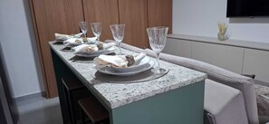 Une table à manger dressée avec des assiettes, des verres et des serviettes, avec une télévision et un vase en arrière-plan.