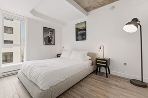 A bedroom with a bed, a nightstand, a floor lamp, a window, and two wall-mounted pictures. - Secret Agent Suite | Rooftop Pool | Sleeps 6 (Québec)