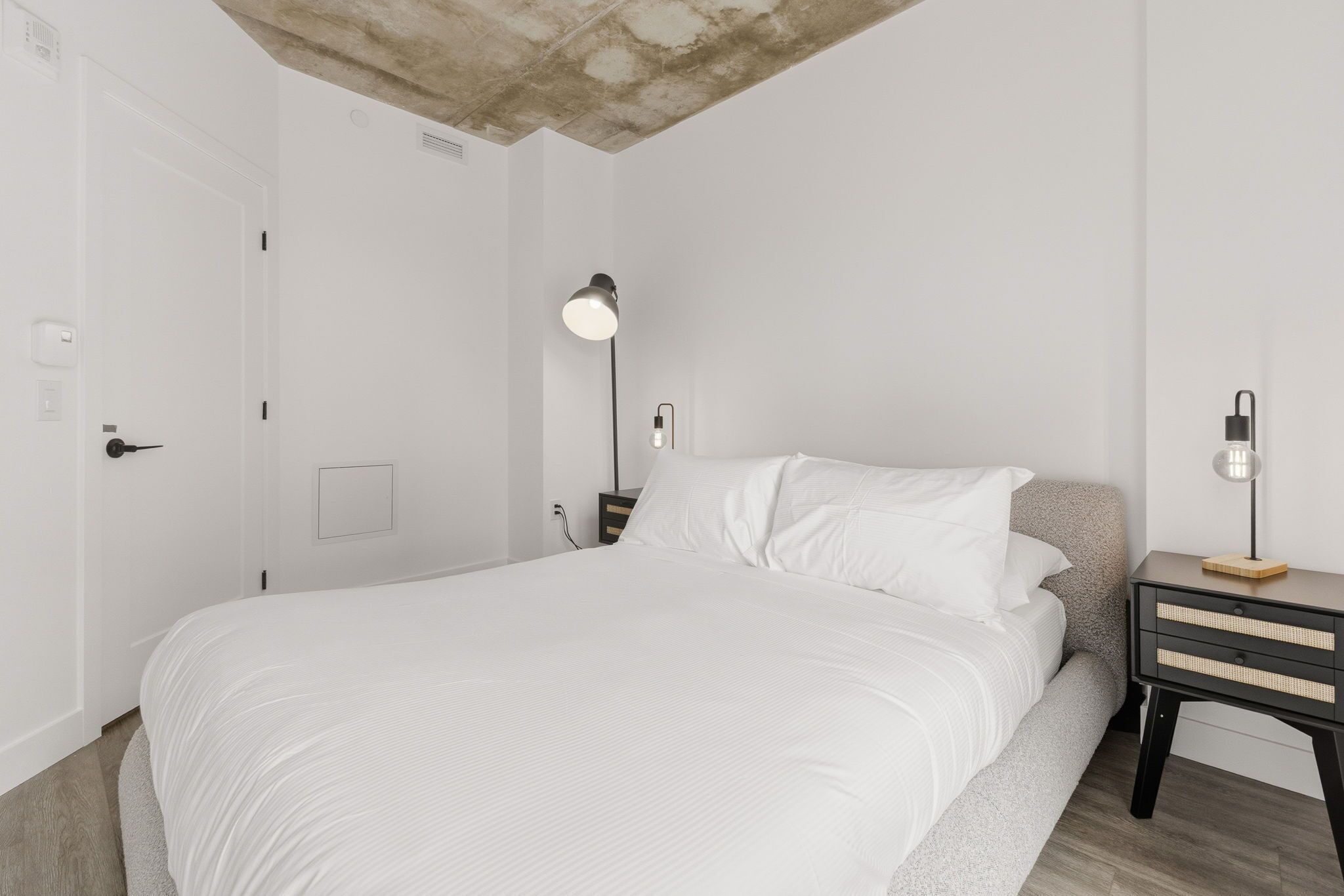 A minimalist bedroom with a bed, bedside tables, and a ceiling light fixture.