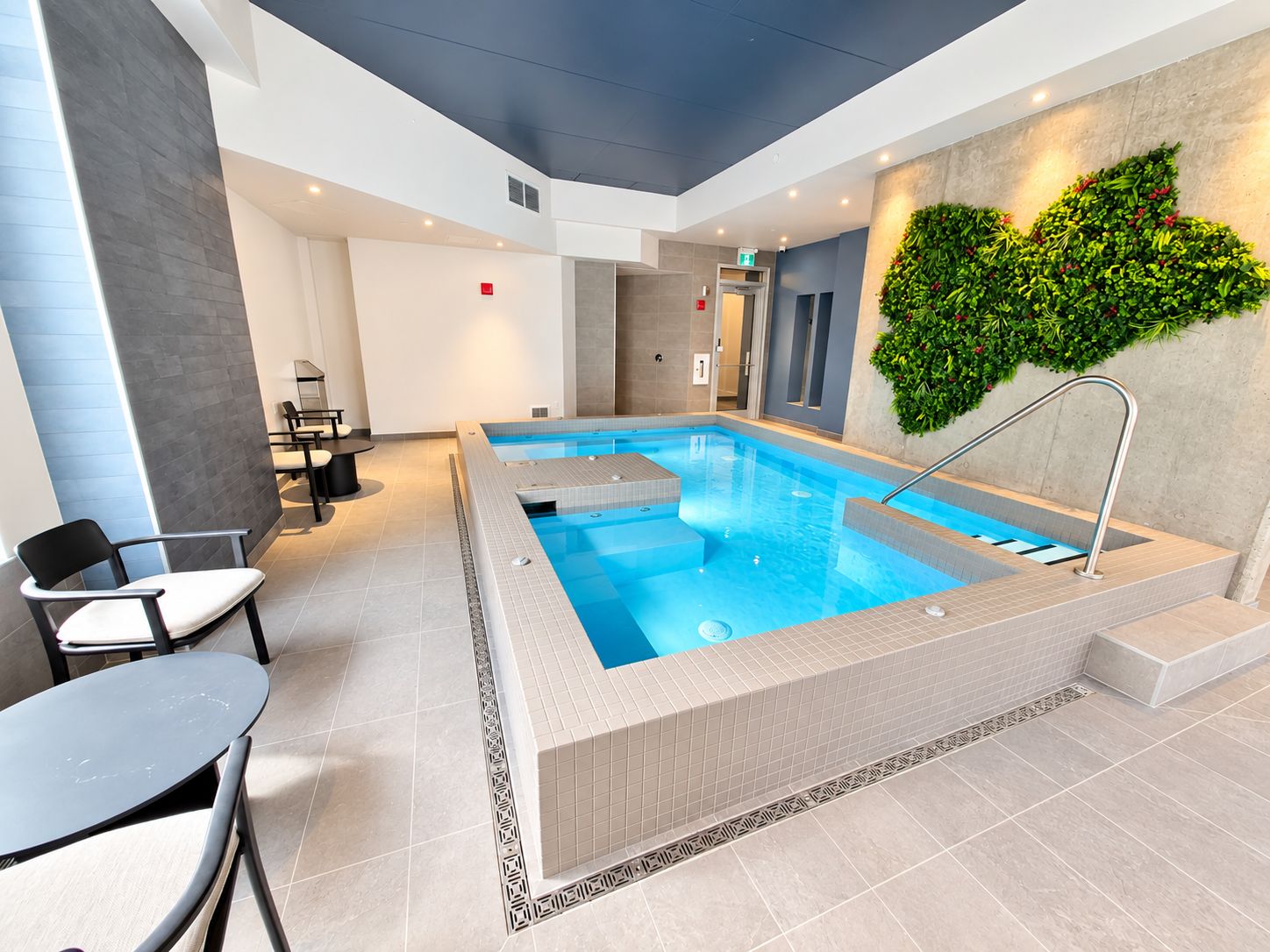 Ein moderner, überdachter Schwimmbereich mit klarem Wasserblick, umgeben von Sitzgelegenheiten und einer dekorativen Wand.