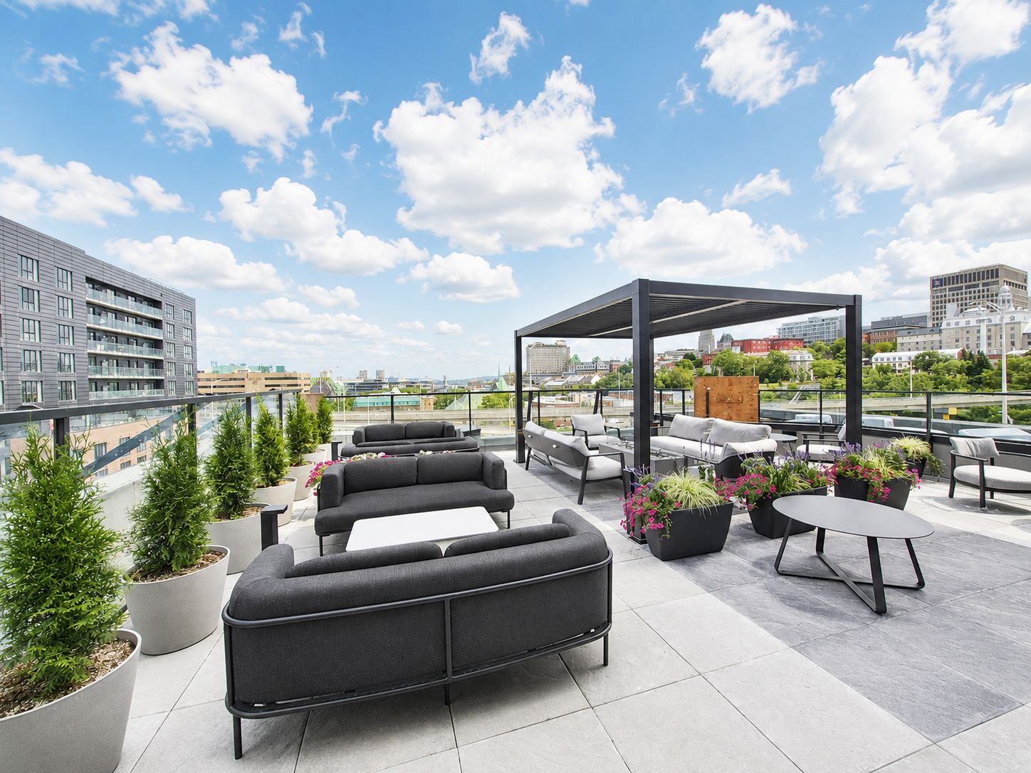 Eine Dachterrasse mit Sitzgelegenheiten im Freien, Topfpflanzen und Blick auf die Skyline der Stadt.