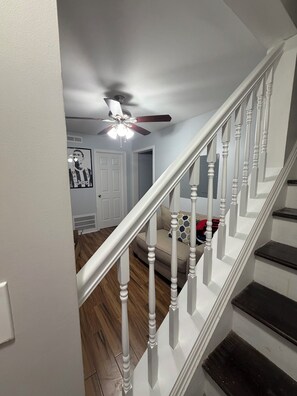 A staircase with white balusters and a ceiling fan in a room with wooden flooring and a door with a vent.