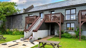 A two-story building with a stone facade, a wooden staircase, and a small garden area with a picnic table. - Romantic Lyme Regis Couple's Hideaway (Bude)