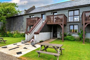 A two-story building with a stone facade, a wooden staircase, and a small garden area with a picnic table. - Romantic Lyme Regis Couple's Hideaway (Bude)