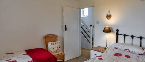 A bedroom with two single beds, a chair with a cushion, a bedside table with a lamp, and a staircase leading to another room.