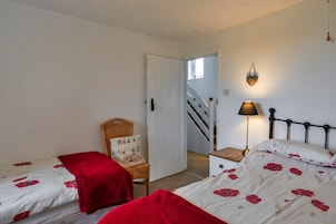 Un dormitorio con dos camas individuales, una silla con cojín, una mesita de noche con lámpara y una escalera que lleva a otra habitación.