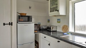 A compact kitchen with white cabinets, a microwave, a toaster, and a wooden cutting board. - Romantic Lyme Regis Couple's Hideaway (Bude)