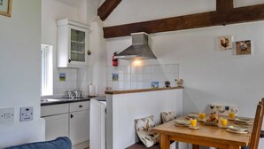 A kitchen with white cabinets, a stove, a sink, and a dining area with a table set for breakfast. - Romantic Lyme Regis Couple's Hideaway (Bude)