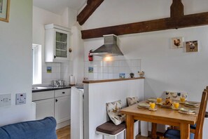 A kitchen with white cabinets, a stove, a sink, and a dining area with a table set for breakfast. - Romantic Lyme Regis Couple's Hideaway (Bude)