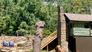 A rustic cabin with a stone chimney, wooden staircase, and a view of a forested area. - Timber N Current -Reopening! (Henderson County)