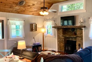A cozy living room with a fireplace, wooden walls, and a television. - Timber N Current -Reopening! (Henderson County)