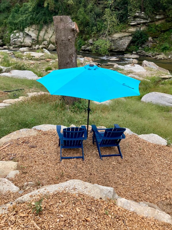 Two Adirondack chairs with a blue umbrella in a natural setting. - Timber N Current -Reopening! (Henderson County)