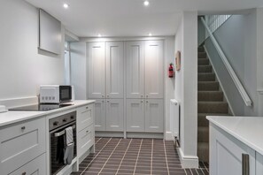 A compact kitchen with white cabinets, a microwave, an oven, and a tiled floor. - Coastal Family House for 6 (Bude)