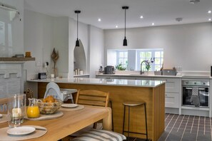 Una cocina moderna con una isla central, un comedor con mesa de madera y vistas al exterior a través de amplios ventanales.