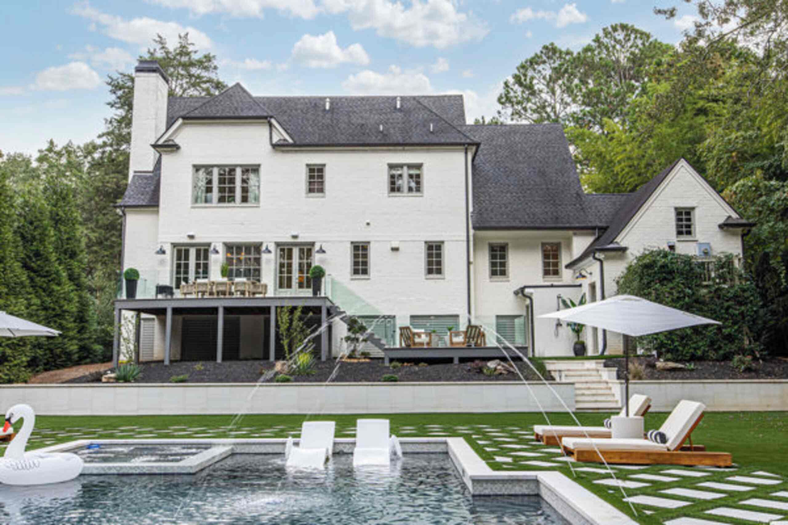 A large white house with a swimming pool, outdoor seating, and a well-maintained lawn.