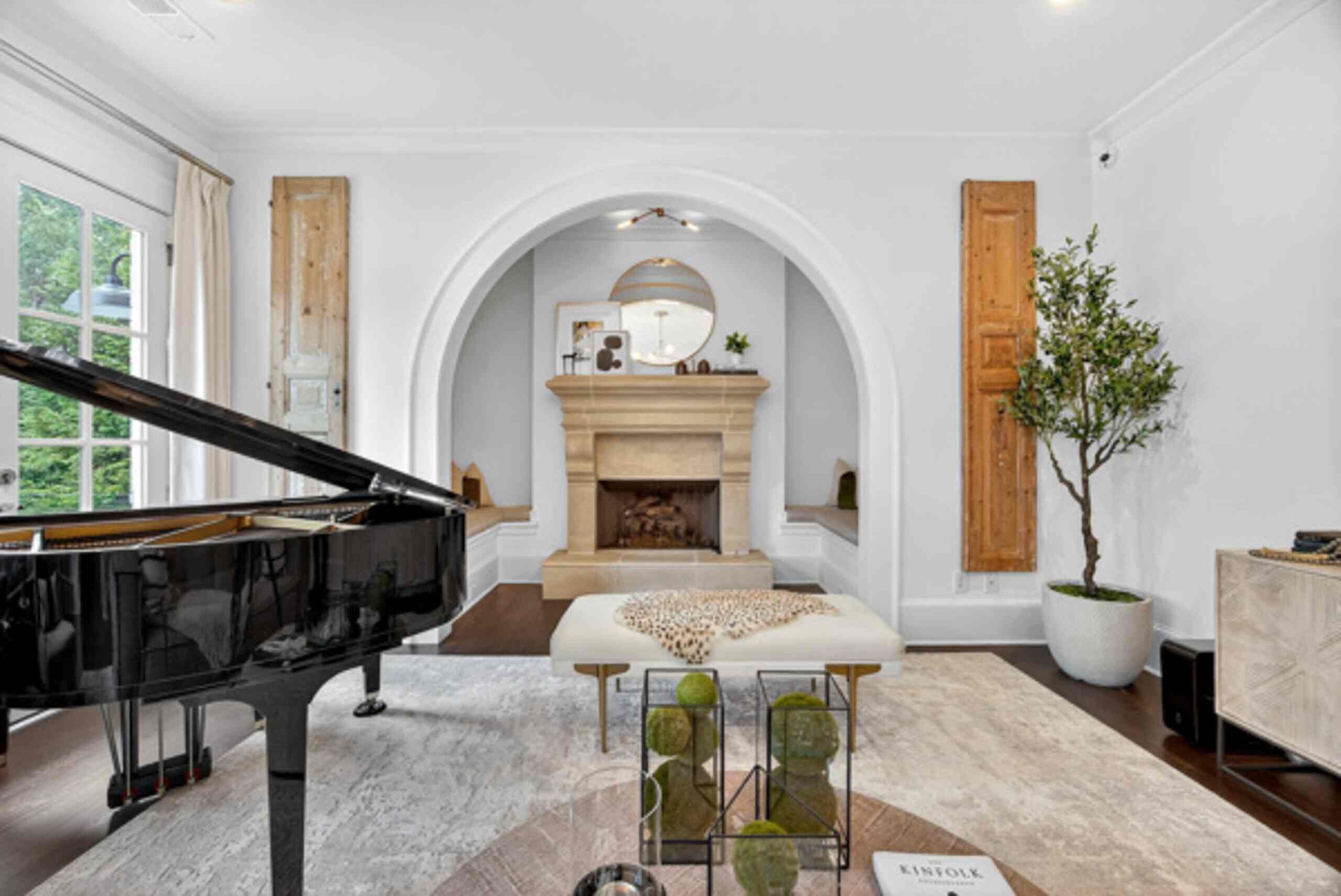 A grand piano in a spacious room with a fireplace, a large mirror, and a potted tree.