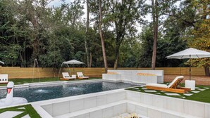 Une piscine dotée d’un jacuzzi intégré, entourée d’une clôture en bois et d’arbres.