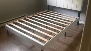 Une chambre avec un cadre de lit, une tête de lit et une fenêtre laissant entrer la lumière du jour.