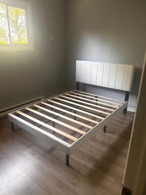 Ein Zimmer mit einem Bettgestell, einer Kopfteil und einem Fenster mit Tageslicht.