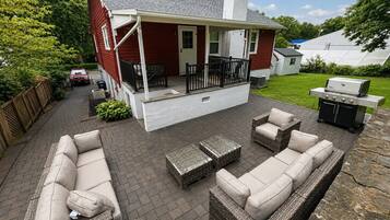 Une terrasse couverte avec des meubles d’extérieur, un barbecue et une maison en arrière-plan.