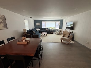 Una sala de estar moderna con un sofá azul oscuro, una mesa de comedor de madera y un televisor de pantalla plana montado en la pared.