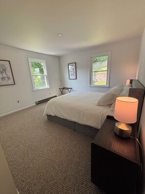 Ein Schlafzimmer mit einem Bett, einem Nachttisch, einer Lampe und zwei Fenstern.
