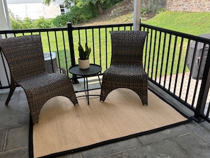 Eine Terrasse mit zwei Korbstühlen, einem kleinen runden Tisch und einem Blumentopf.
