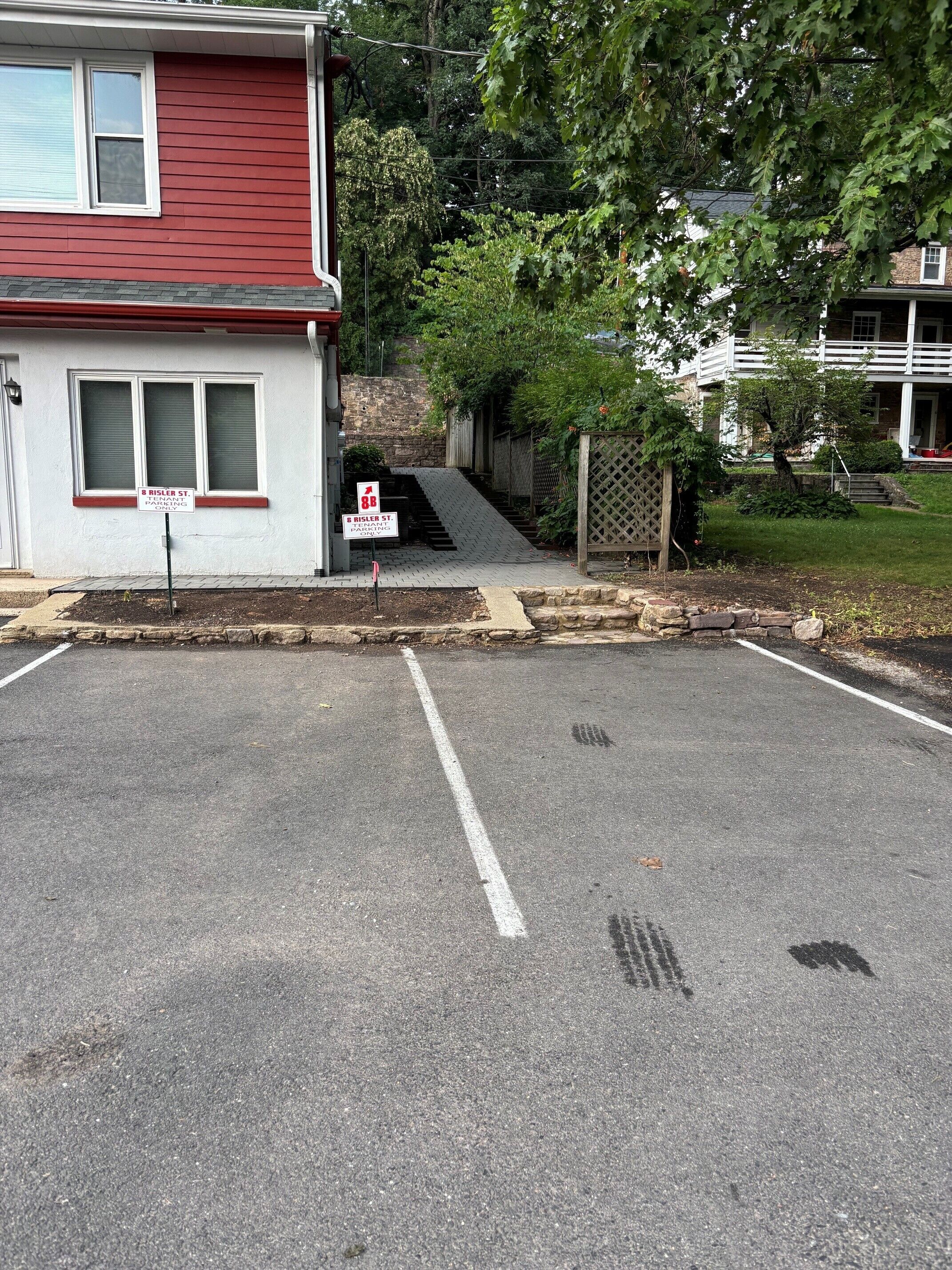 Un parking délimité par une ligne blanche, un bâtiment rouge avec une fenêtre blanche et un panneau indiquant : « 8, rue Risler, stationnement réservé aux locataires ».