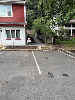 Un estacionamiento con una línea blanca que marca el borde, un edificio rojo con un ventanal blanco, y un letrero que indica '8 RISLER ST. SOLO ESTACIONAMIENTO PARA INQUILINOS'.