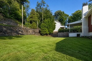 Ein Wohngrundstück mit einer Steinmauer, einer Rasenfläche und einem weißen Haus mit einer Veranda.