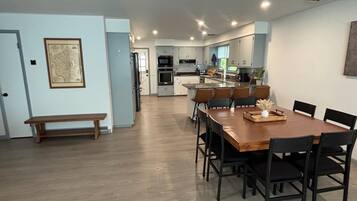 A spacious dining area with a long wooden table and black chairs, a bench, and a kitchen in the background.