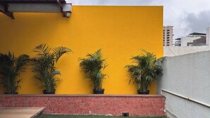 A courtyard with a yellow wall, potted plants, a blue mat, and a brick wall.