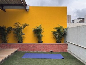 A courtyard with a yellow wall, potted plants, a blue mat, and a brick wall.